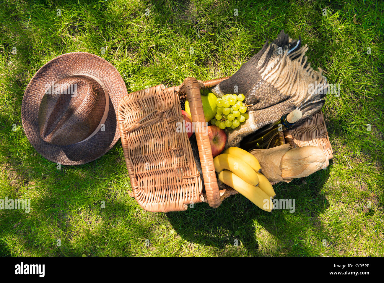 Top view of wicker picnic basket with fruits and wine bottle on green ...