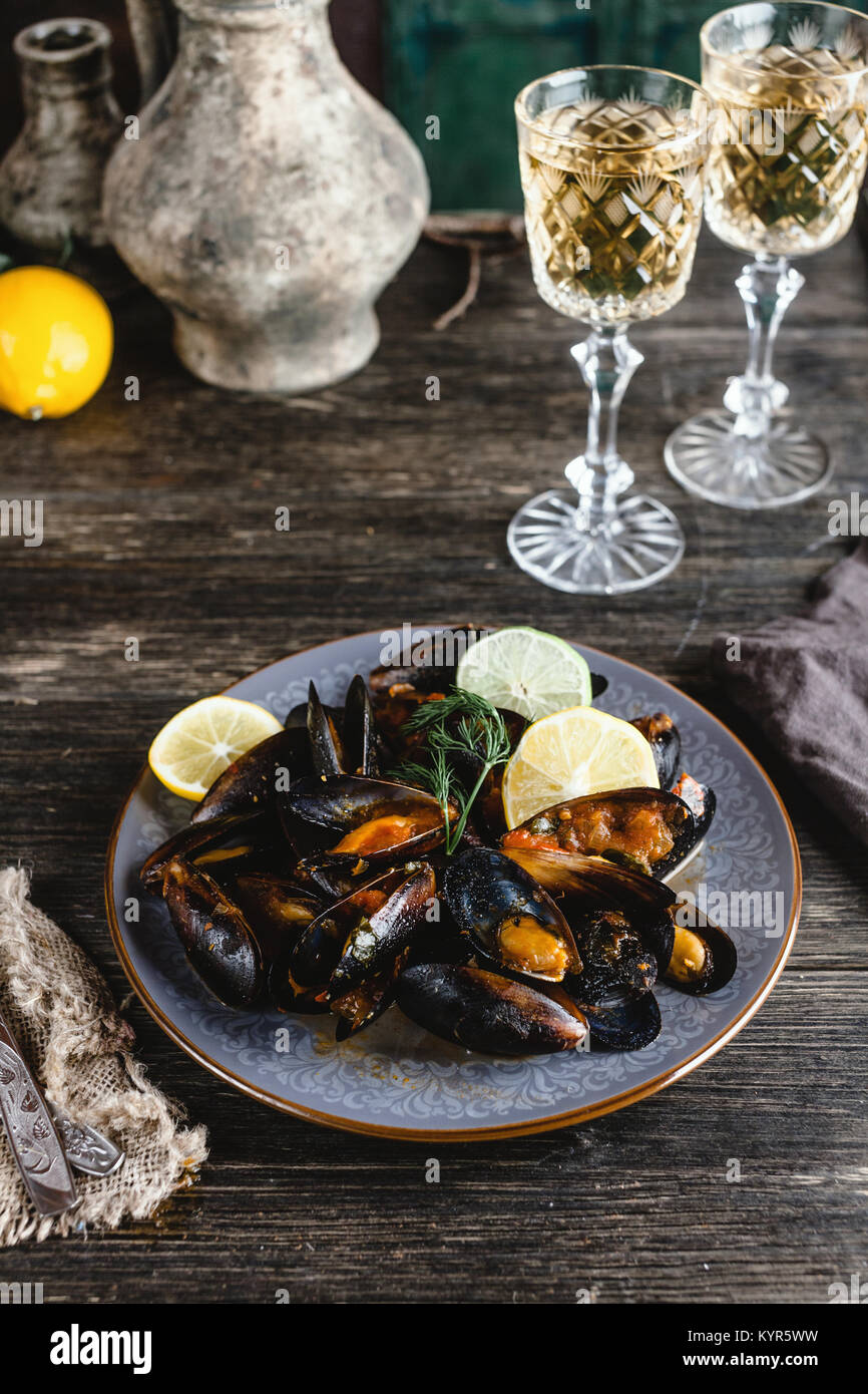 Cooked mussels with shells served on plate with two glasses of white wine on wooden table Stock Photo