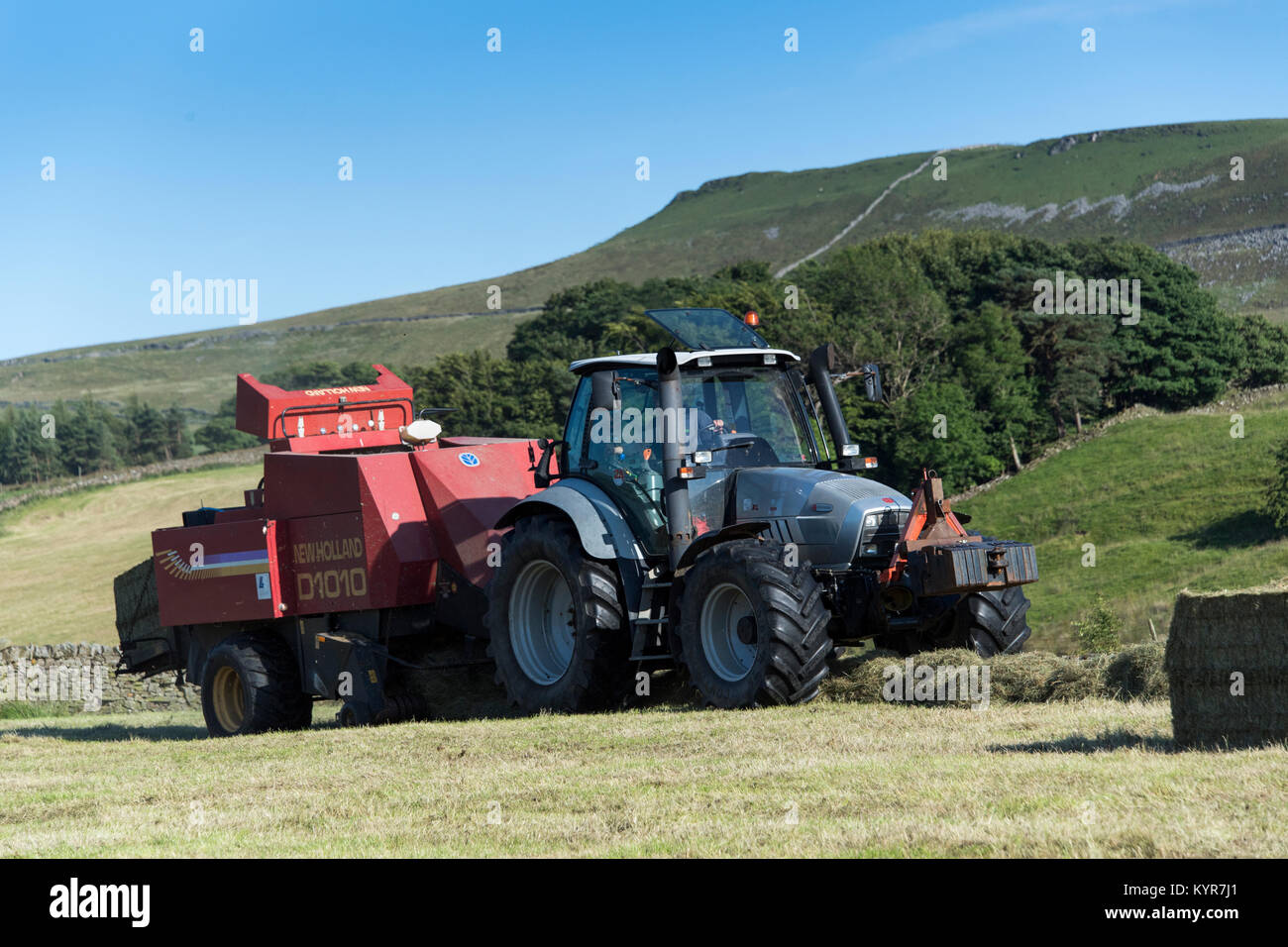 Baling a field of hay in the Yorkshire Dales with a large square baler and Hurlimann tractor. Stock Photo