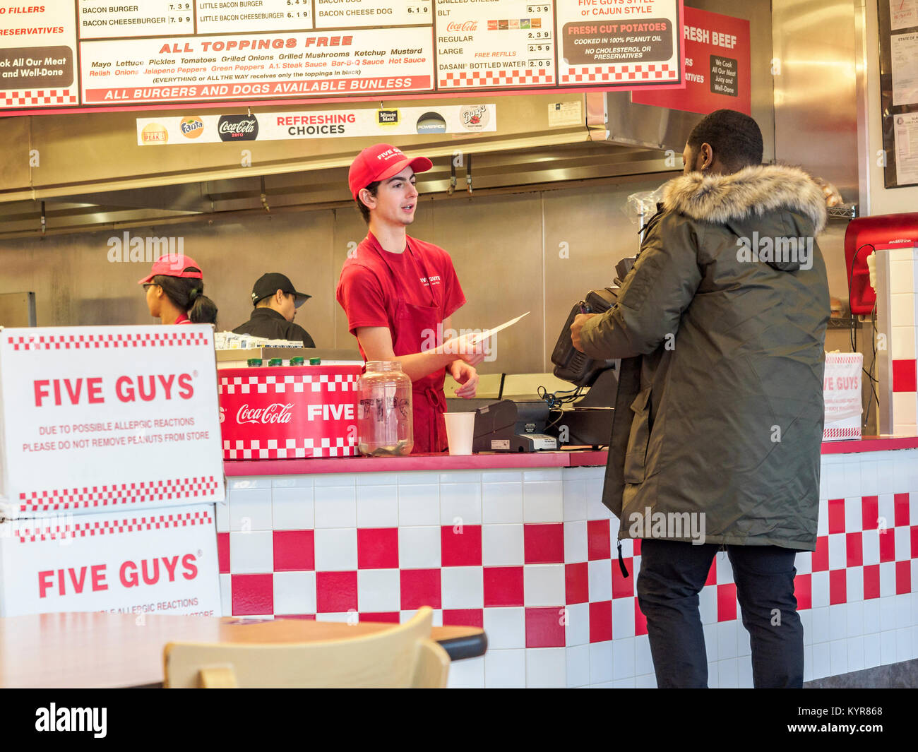 Fast food worker at the counter helping an African-American male customer order food at Five Guys a hamburger restaurant in Montgomery Alabama, USA. Stock Photo