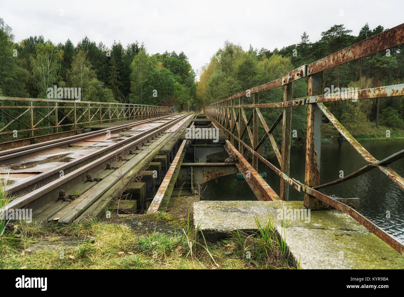 Old abandoned railroad bridge above river in Poland; vintage motorbike in background. Vintage industrial landscape Stock Photo