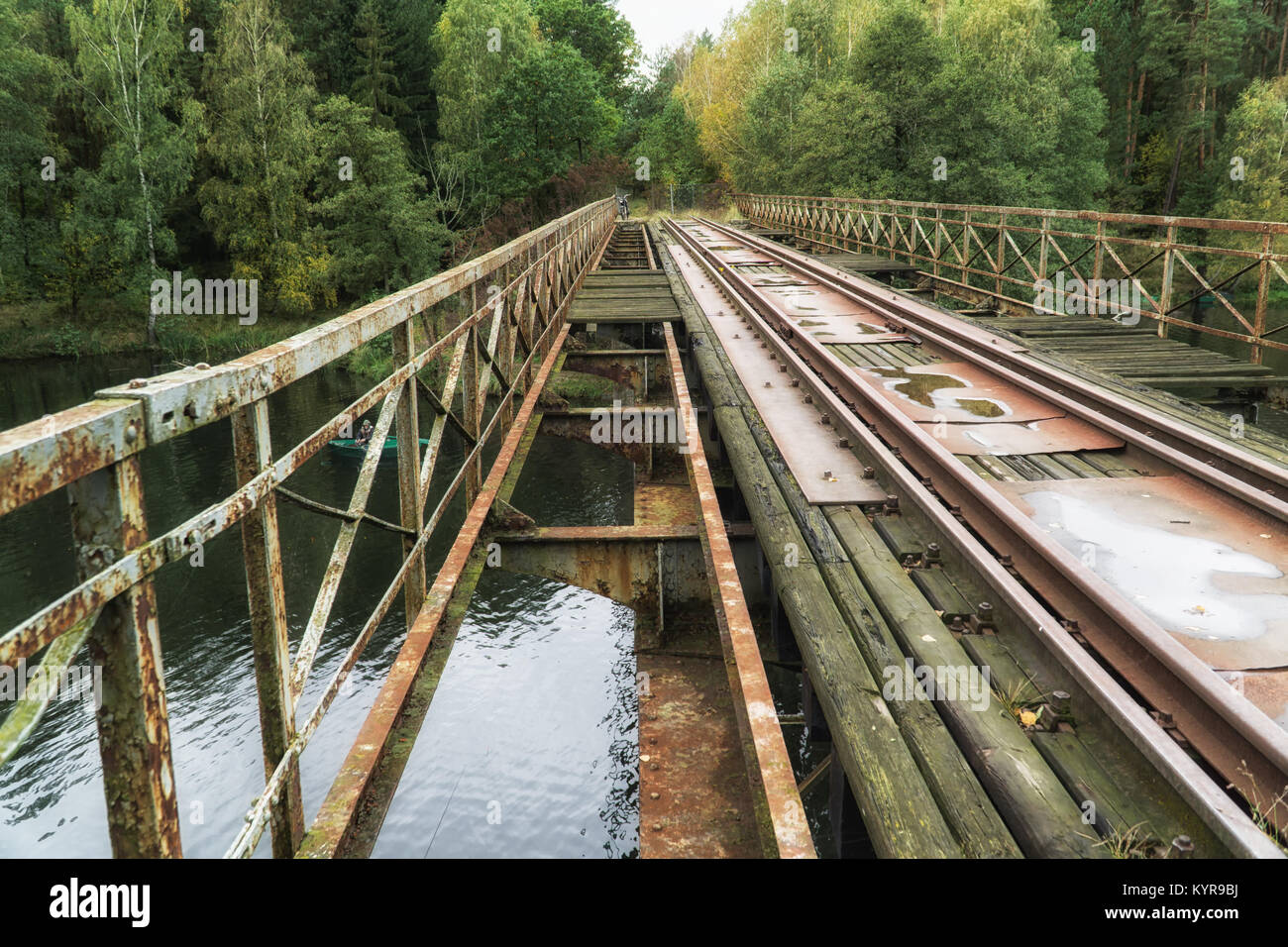 Old abandoned railroad bridge above river in Poland; vintage motorbike in background. Vintage industrial landscape Stock Photo