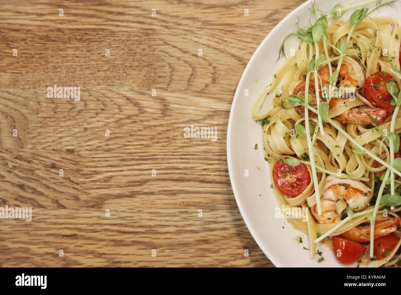 half of a white dish with shrimp scampi and linguini in  on a wood table from top view Stock Photo