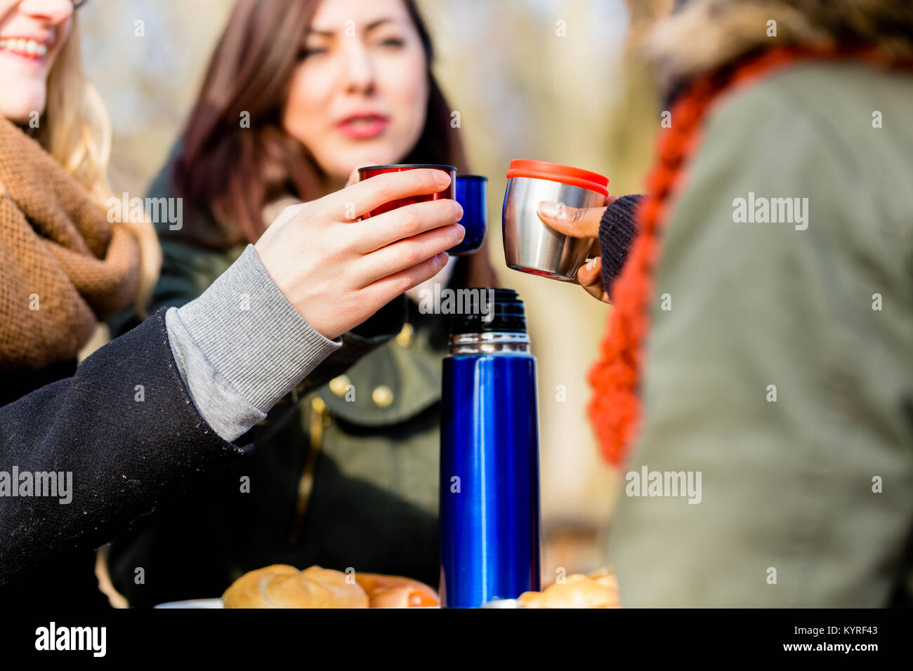 Young female friends drinking a hot beverage outdoors in winter Stock Photo