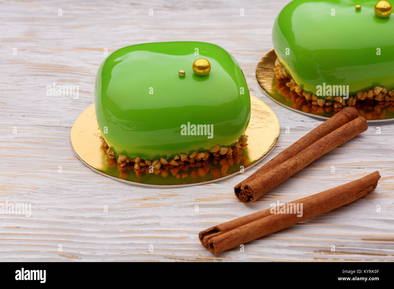 Green Mousse cakes with cinnamon sticks on wooden white background. A modern dessert Stock Photo