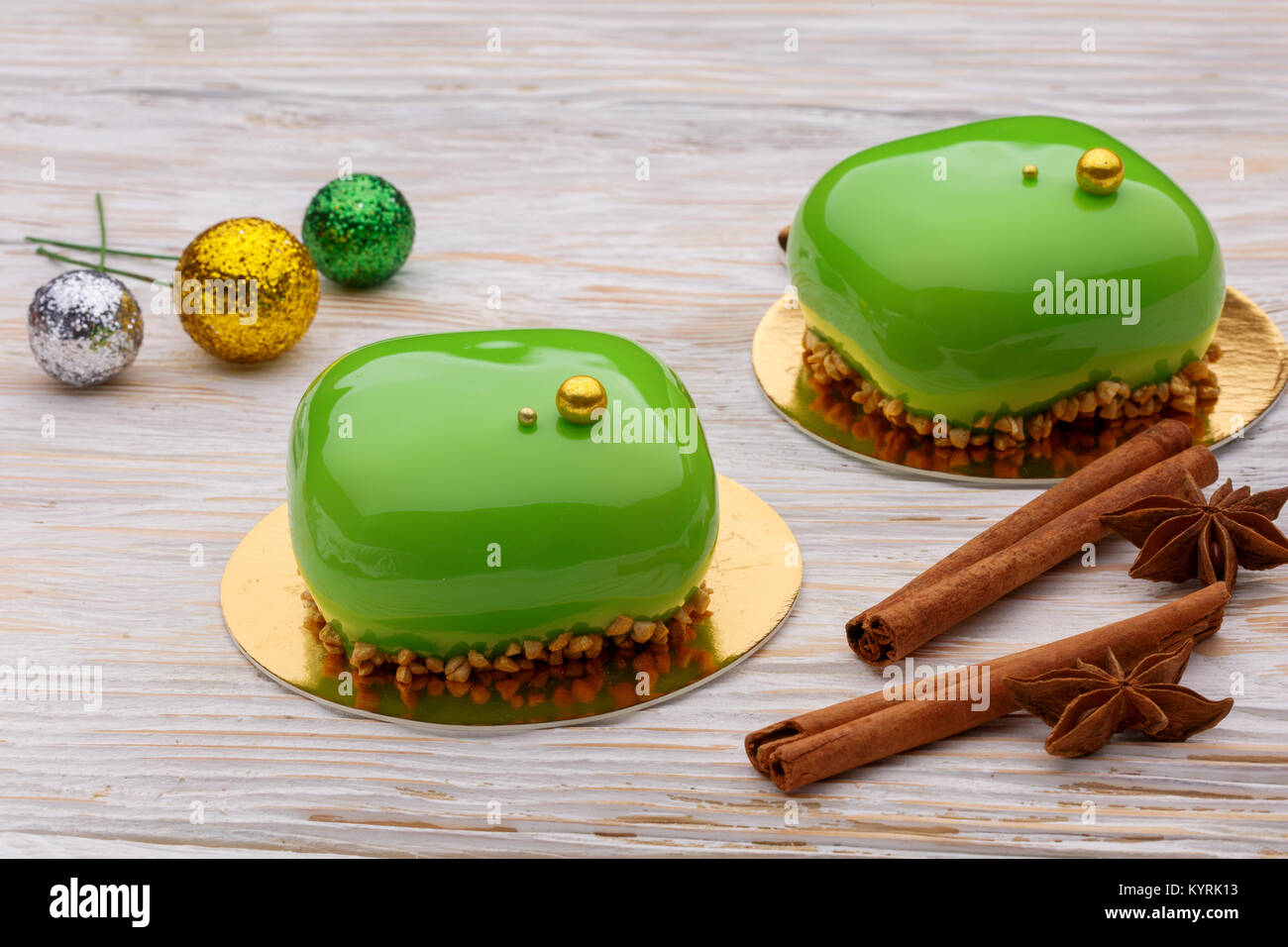 Green Mousse cakes with cinnamon sticks on wooden white background and shiny Christmas balls. A modern dessert Stock Photo