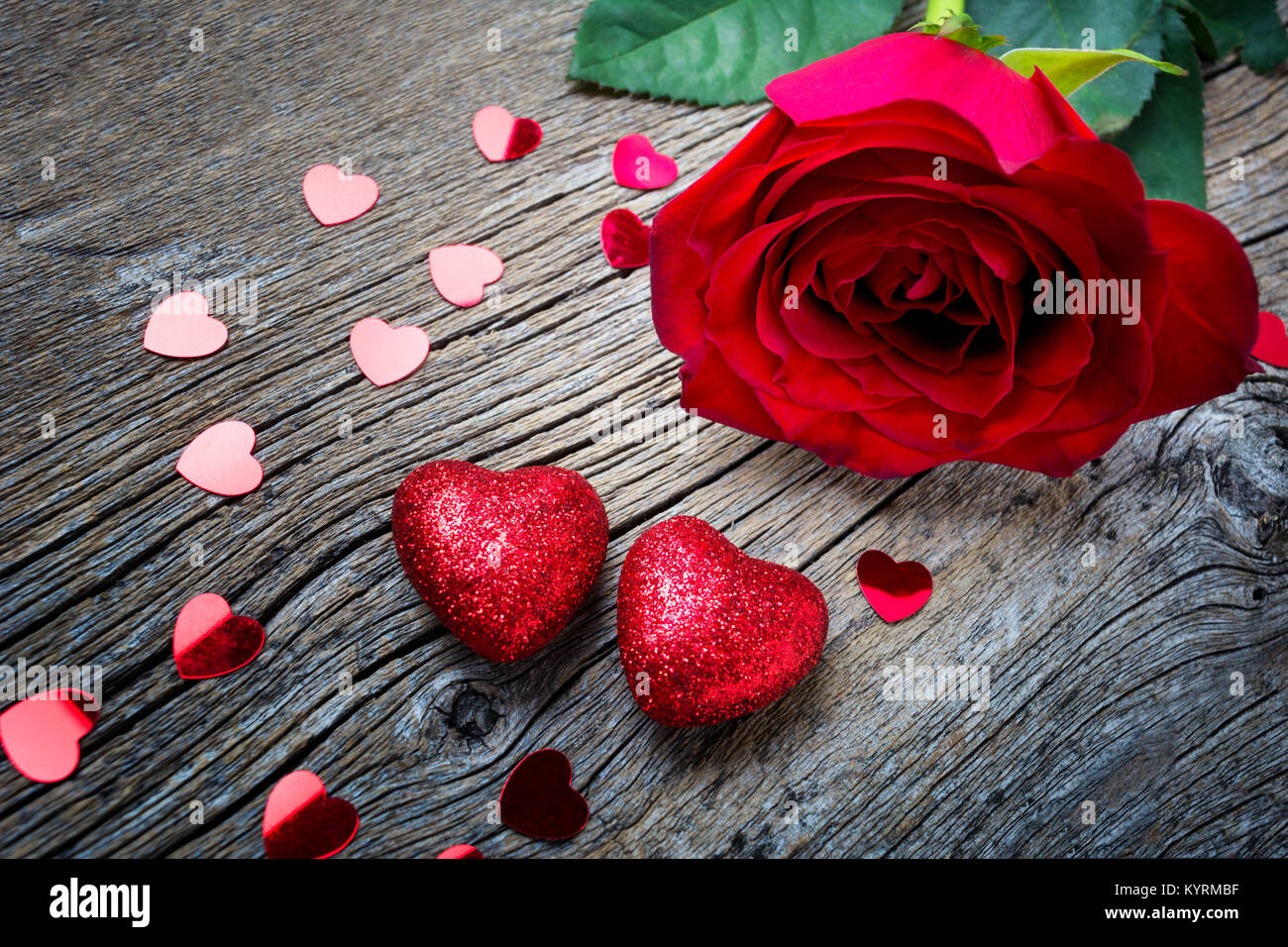 Valentines Day concept with red rose, glitter and paillette hearts on the rustic wooden background, copy space. Stock Photo