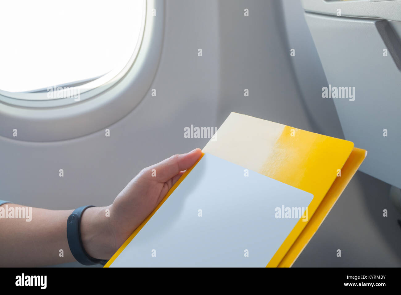 Close up woman hand reading at blank open leaflet when flying at window seat in airplane ,mock up for adding your design. Stock Photo