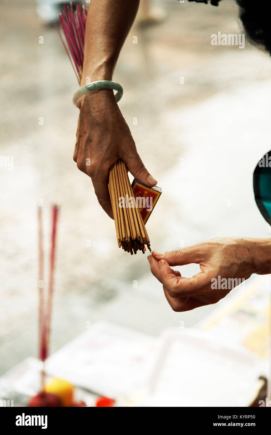 Woman holding large burning incense sticks while praying at chinese