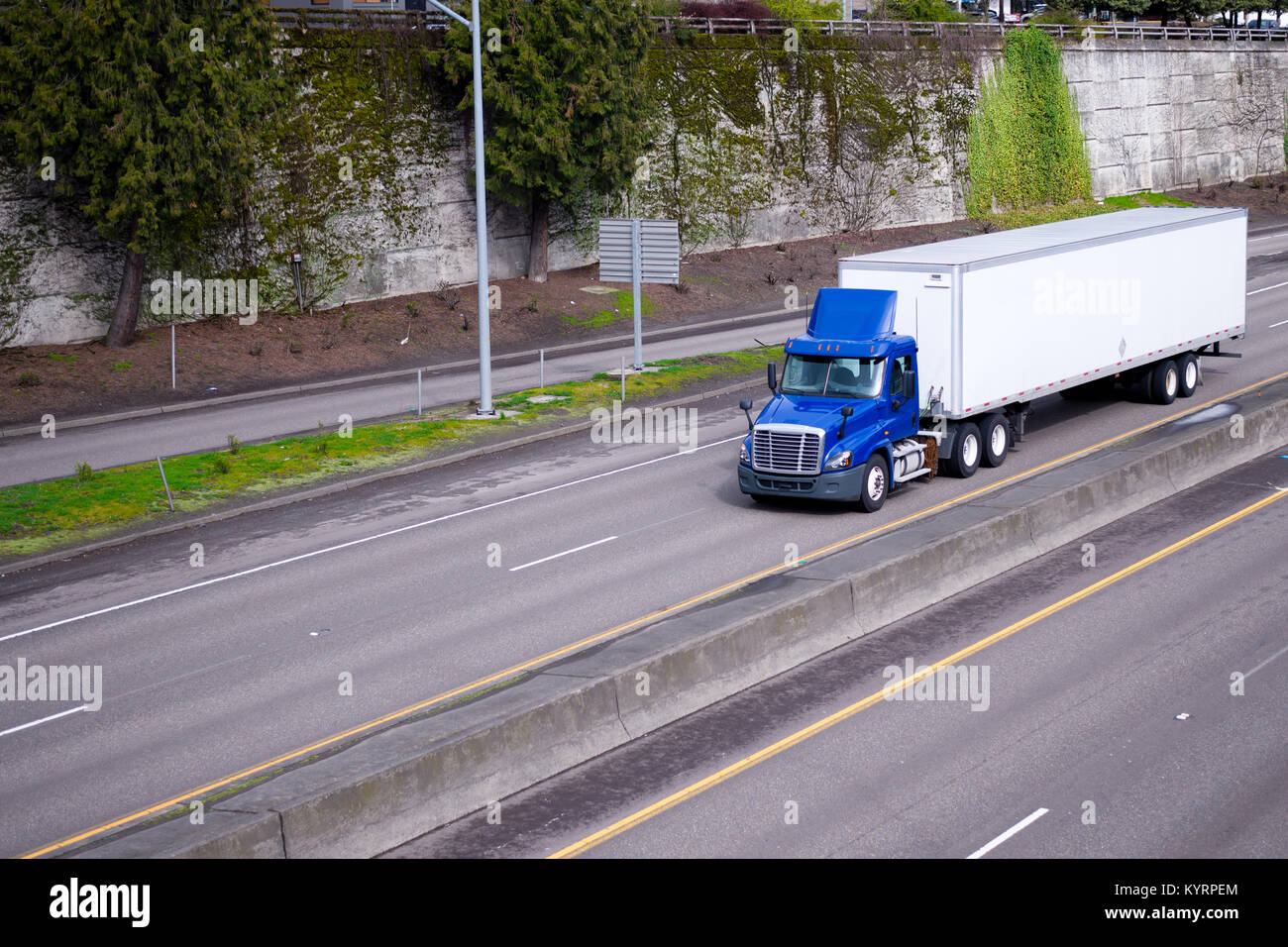 A blue semi truck with day cockpit and a roof spoiler to reduce air resistance and improve aerodynamics carries the trailer with cargo along the road  Stock Photo