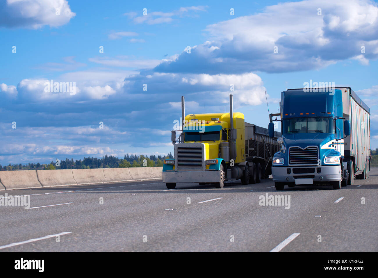 Two semi trucks of various models and manufacturers, a yellow classic American semi truck with a bulk trailer and a blue modern American semi truck Stock Photo