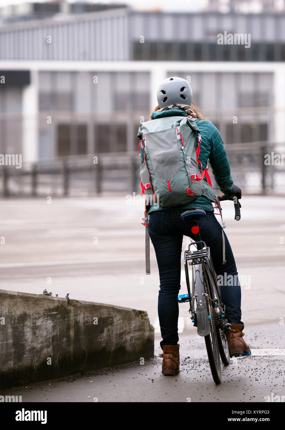 A young girl with long hair in good shape rides in a modern city on a road bike in all outfits and a helmet and with a large backpack behind her shoul Stock Photo