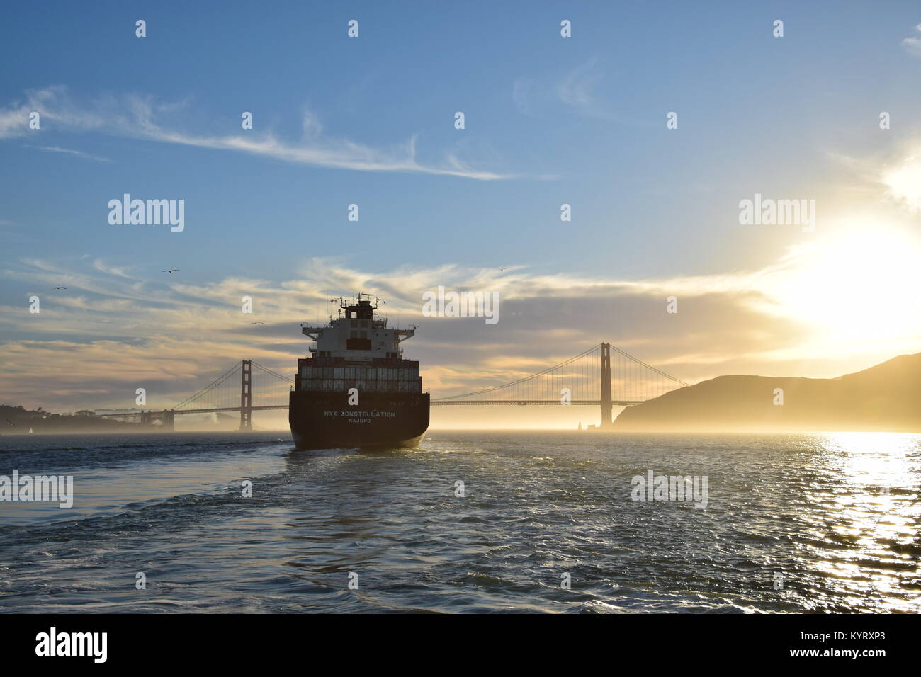 Container ship NYK Constellation leaves San Francisco Bay under the Golden Gate Bridge into the sunset. Stock Photo