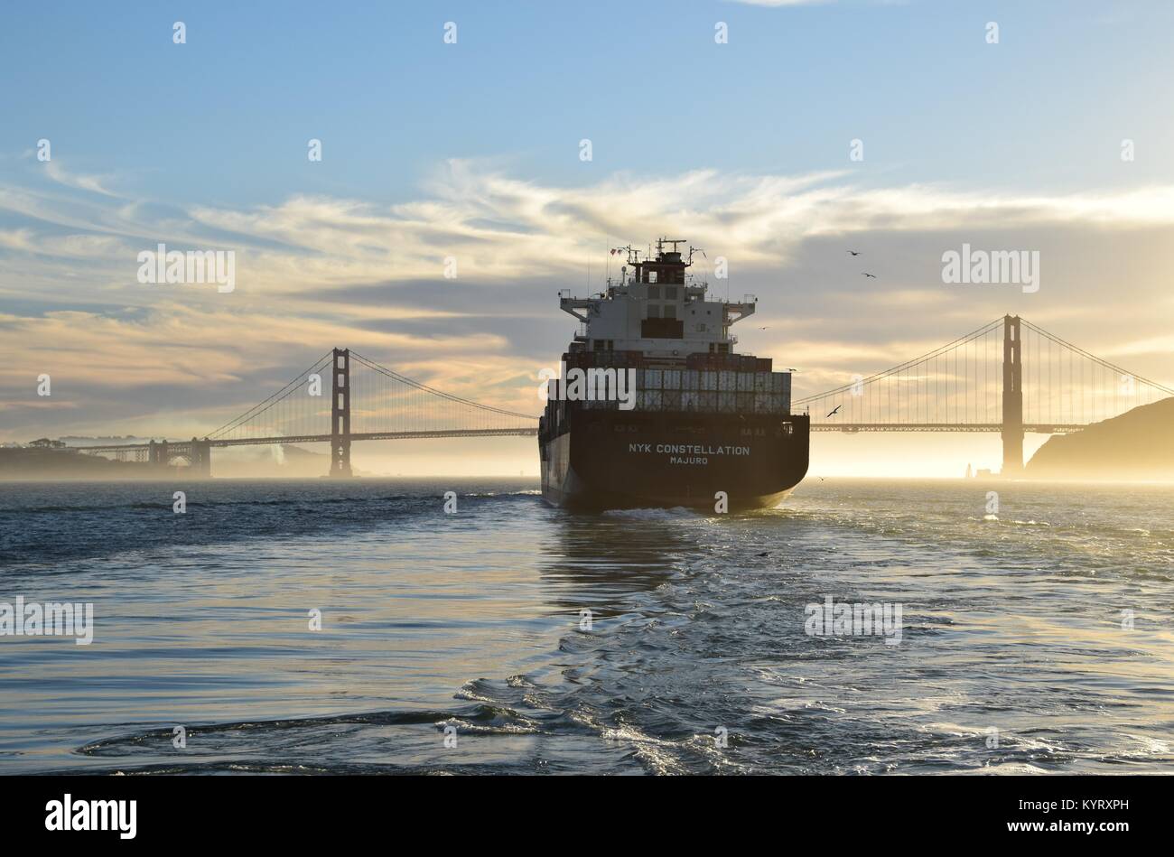 Container ship NYK Constellation leaves San Francisco Bay under the Golden Gate Bridge into the sunset. Stock Photo