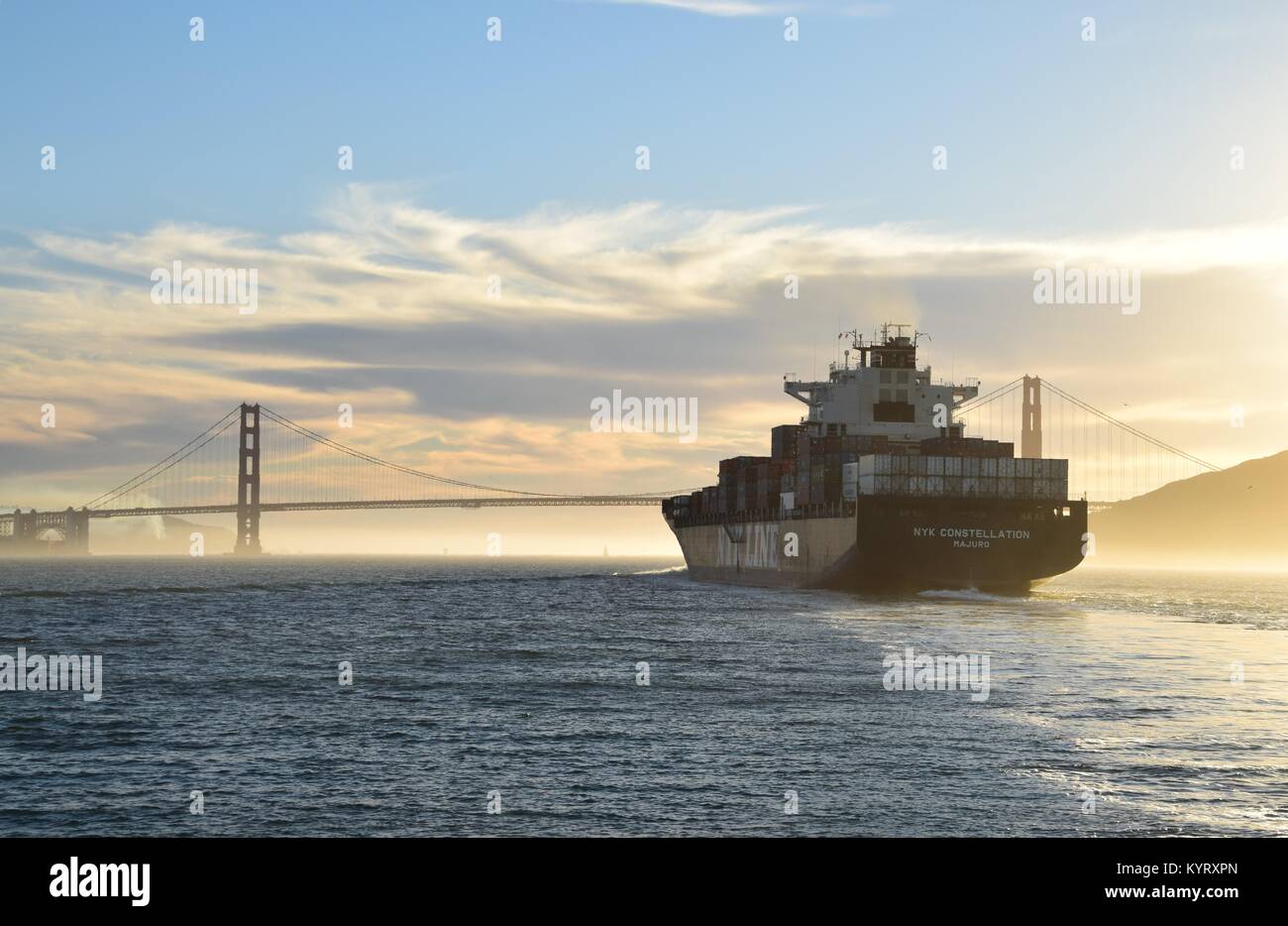 Container ship NYK Constellation leaves San Francisco Bay under the Golden Gate Bridge into the sunset. Stock Photo