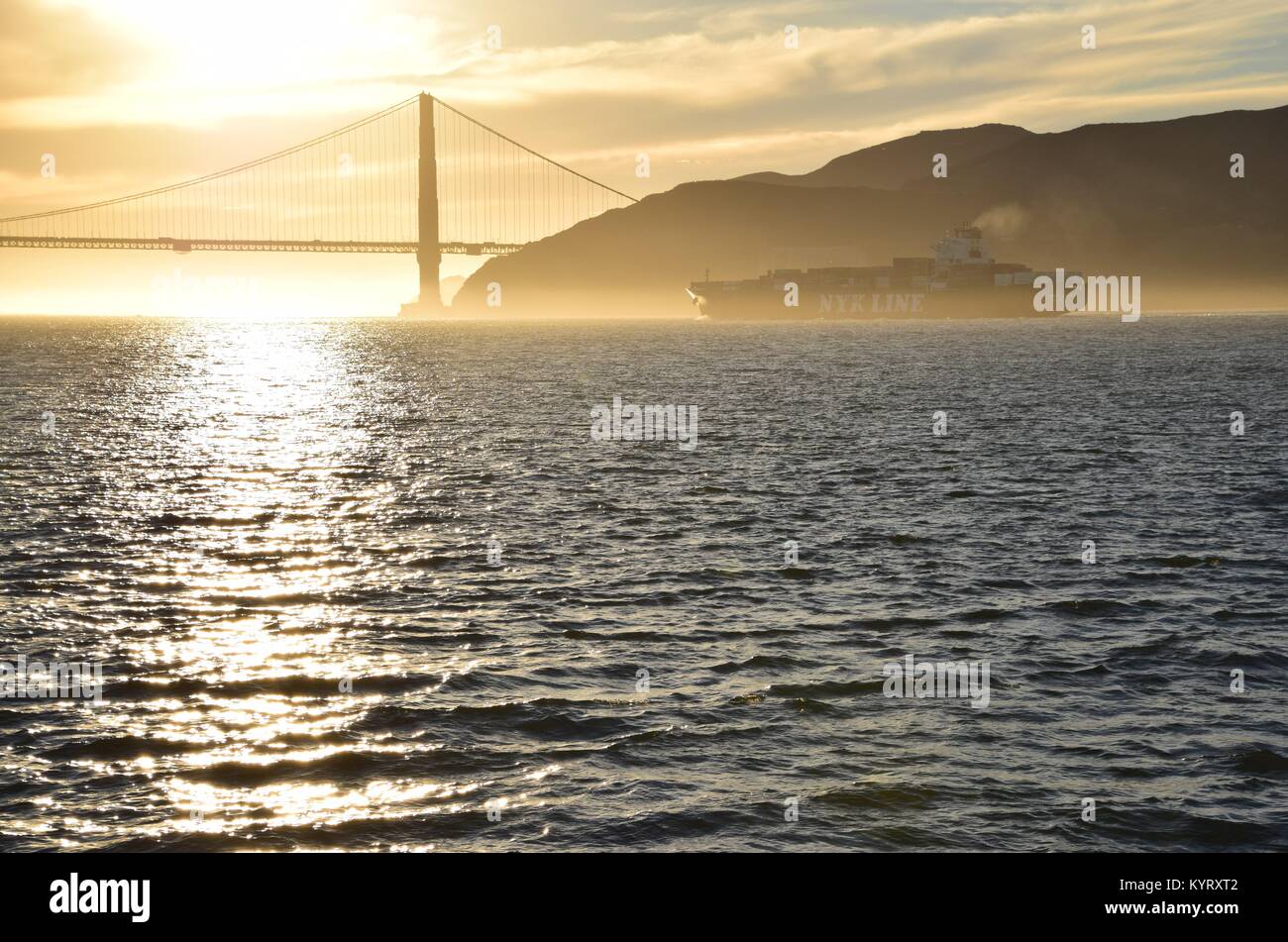 Container ship NYK Constellation leaves San Francisco Bay under the Golden Gate Bridge into the sunset. Stock Photo