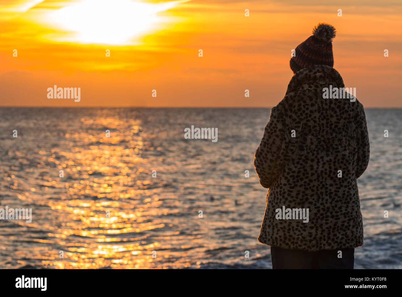 Woman standing by the sea in Winter watching the sunset in the UK. Stock Photo