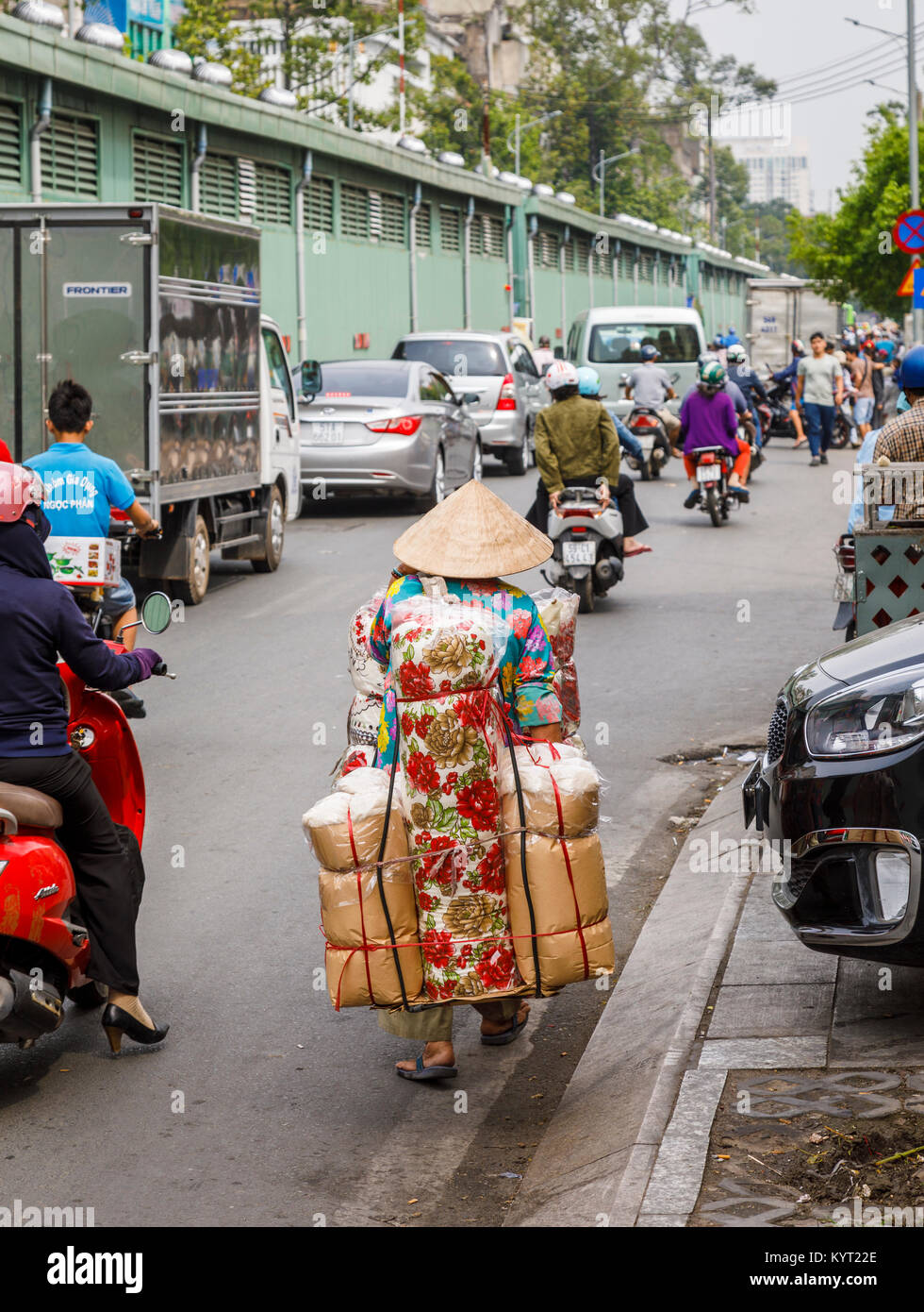 Vietnamese life: woman in conical hat carrying large parcels on her back on a busy road,typical street view in Saigon (Ho Chi Minh City) south Vietnam Stock Photo