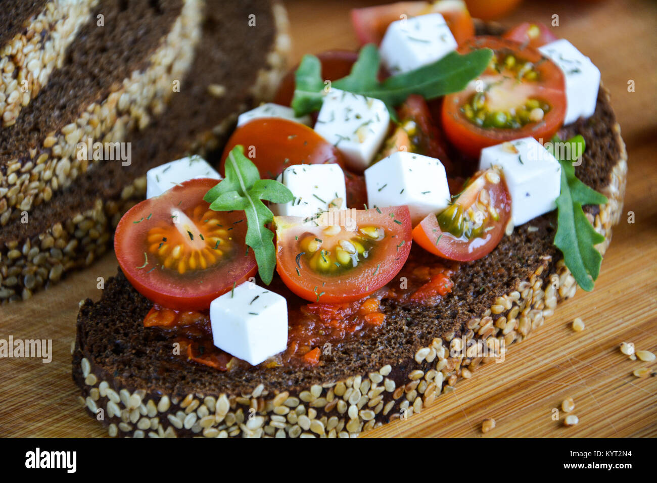 Juicy sandwich with tomato, cheese and herbs on black bread with cereals background Stock Photo