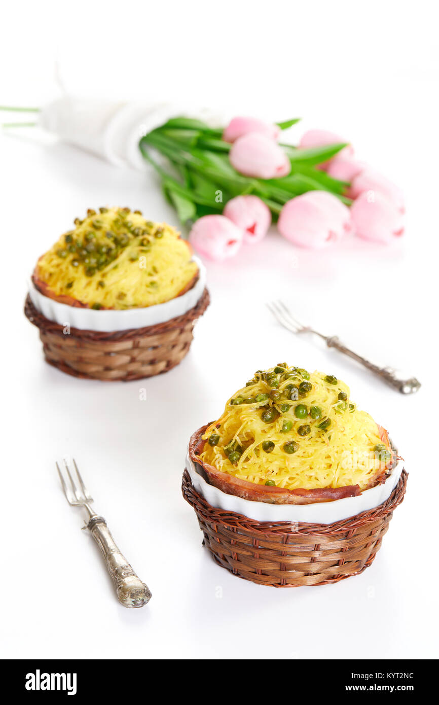 Timbale with tagliolini pasta, peas and ham in ceramic casseroles on white table with pink tulips. White background, spring food. Stock Photo