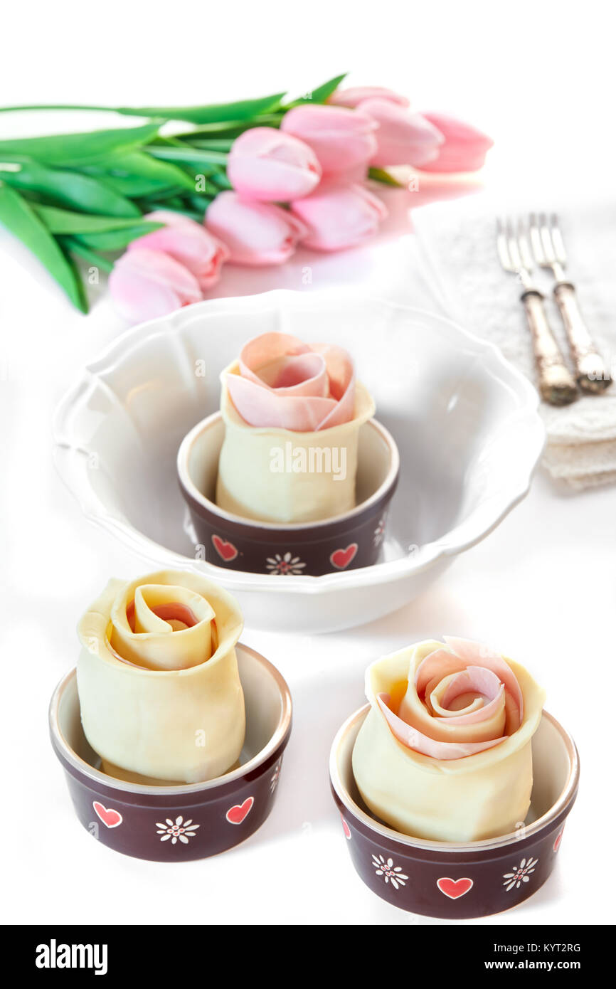 Puff pastry roses with ham and provola cheese in their casseroles, before being baked, on white table with pink tulips. Spring mood. Stock Photo
