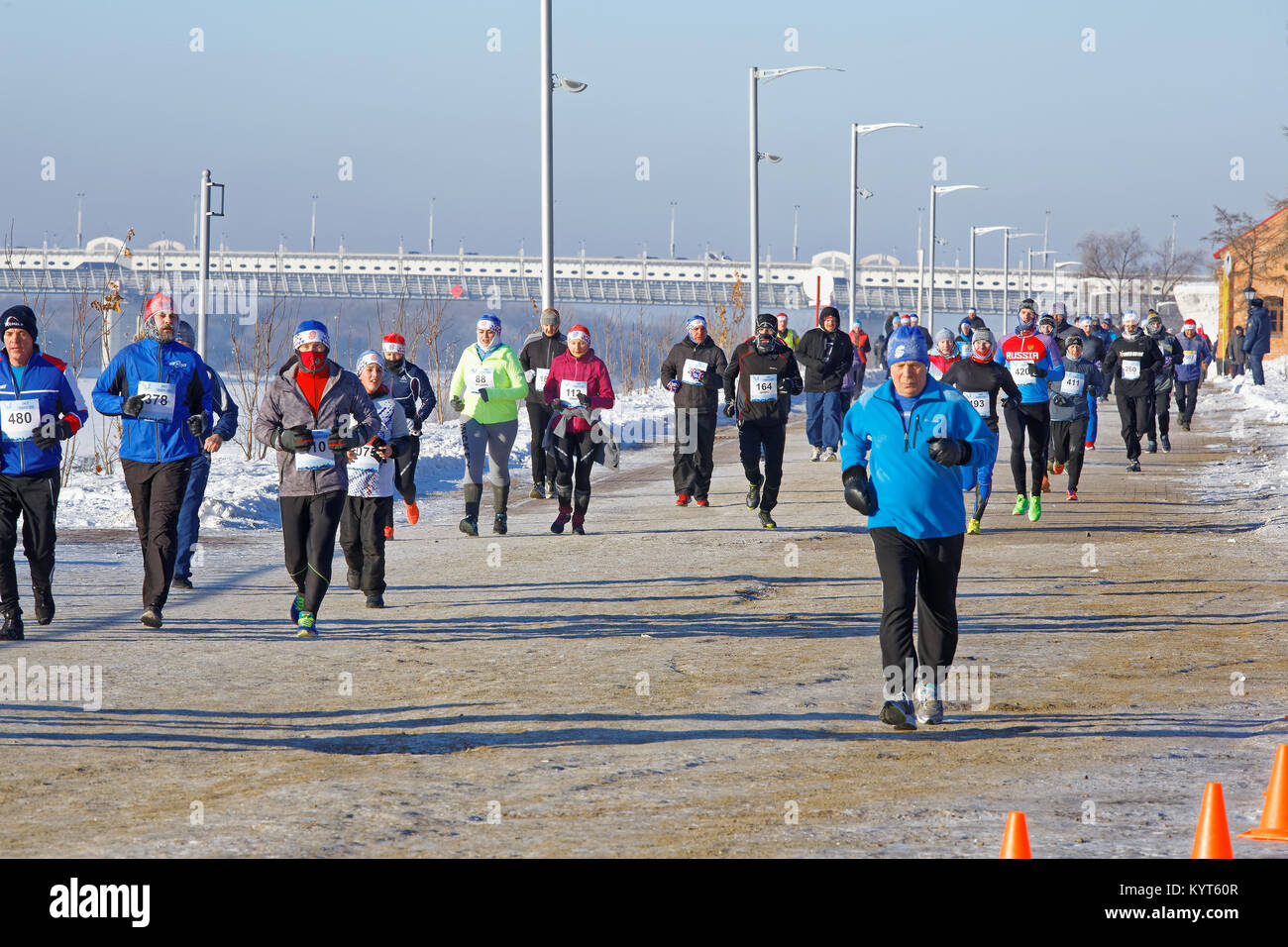Editorial. Omsk, Russia - January 7, 2018. Runners of different age in sports suits run along the street embankment of Tukhachevsky Stock Photo