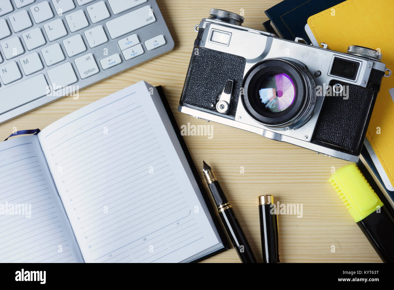 Open note pad, keyboard and vintage photo camera on a wooden desk. Mock-up. Stock Photo
