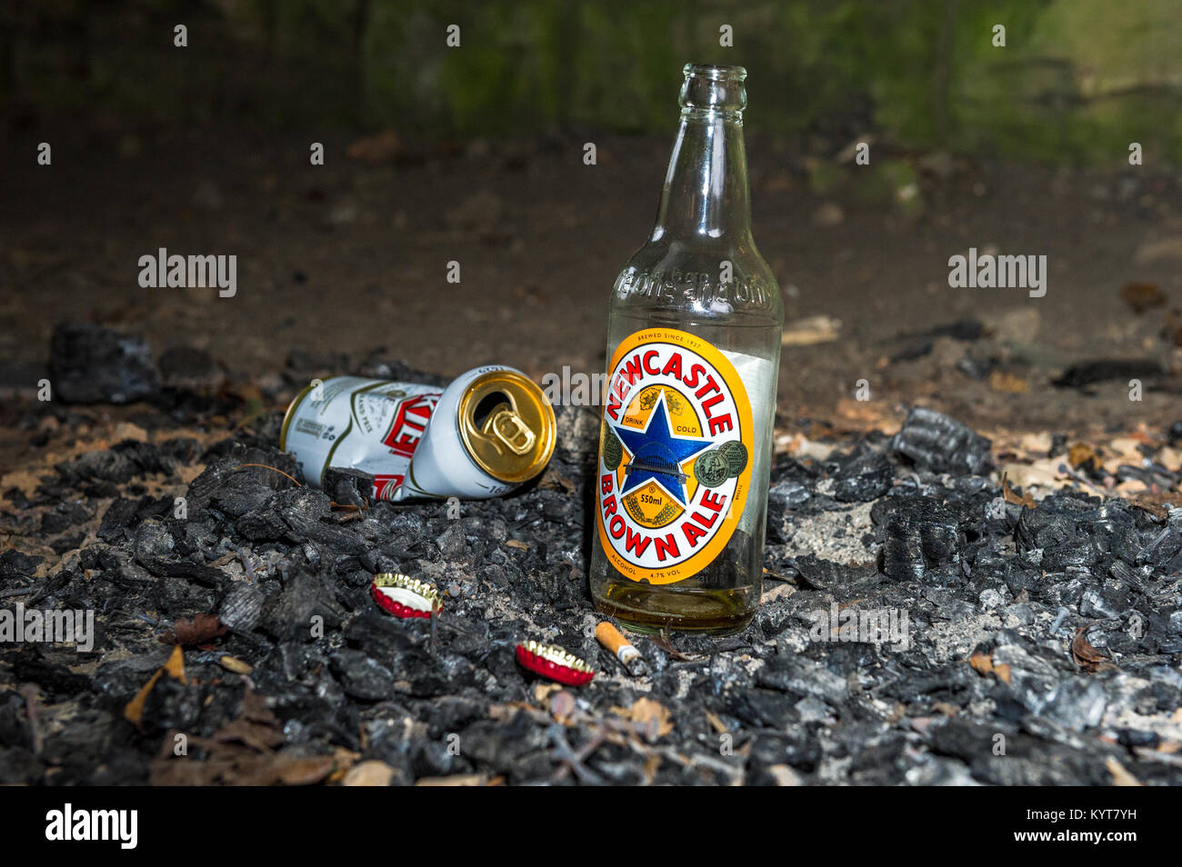 Empty and discarded beer bottle and can in the ashes of a fire. Stock Photo