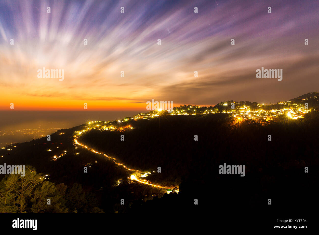 Clouds moving in fast during a beautiful sunset at Mcleodganj, Dharamsala, Himachal pradesh, India. Light Trails of Vehicles climbing up the mountain Stock Photo