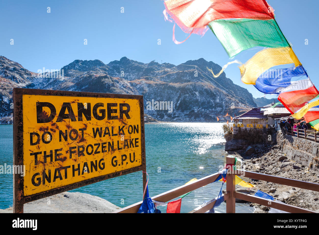 Tsomgo lake / Changu lake near Gangtok city in East Sikkim, North east India. Beautiful Buddhist prayer flags flutter and danger sign board in front Stock Photo