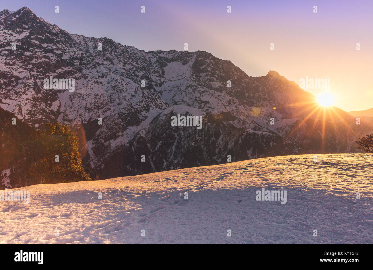 Sun rises over snow capped mountain peaks at Triund, Mcleodganj, Dharamsala, Himachal pradesh, India. Purple/golden hues of Dawn. Surrounded by snow Stock Photo