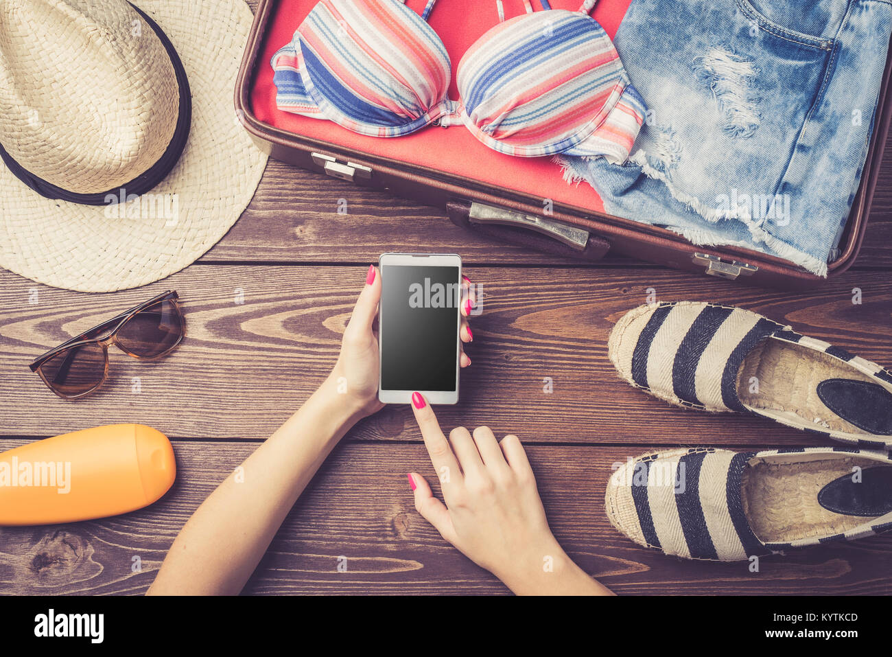 Open suitcase with summer or beach clothes and accessories on wooden