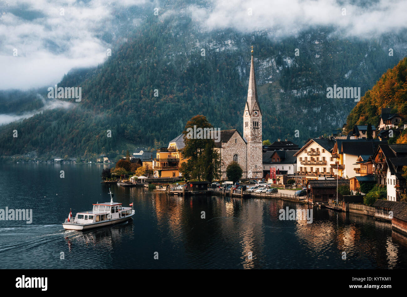 Electric small ferry arrives at the pier of Hallstatt town reflecting in Hallstattersee lake in the Austrian Alps in morning, Salzkammergut region, Au Stock Photo
