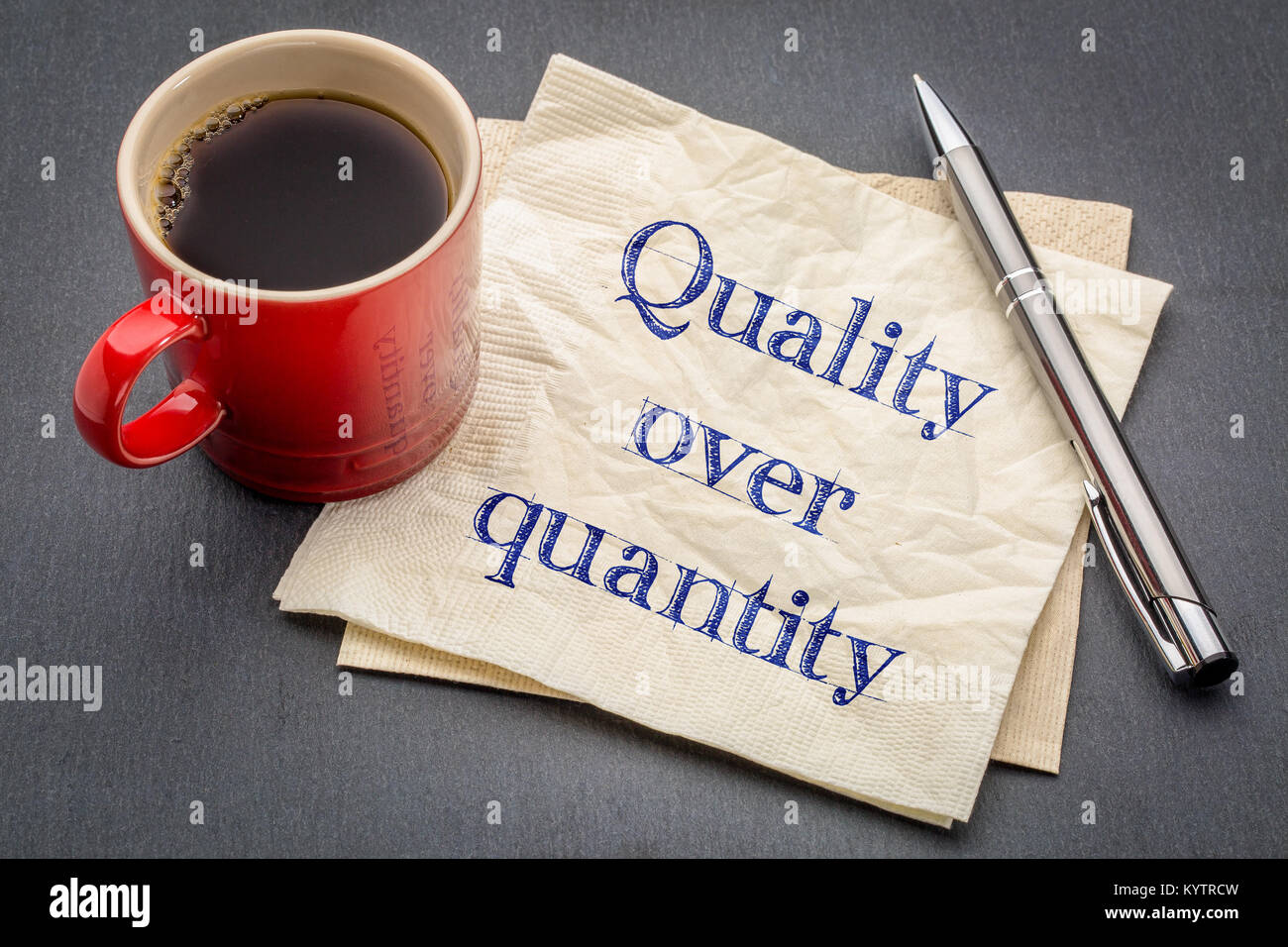 quality over quantity inspirational reminder note - handwriting on a napkin with cup of coffee against gray slate stone background Stock Photo