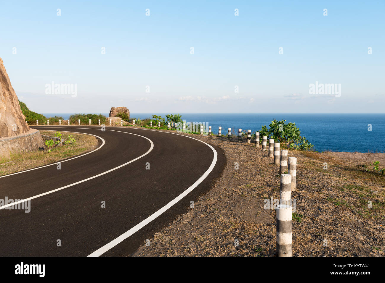 Tarmac coastal road going round cliff edge bend, with blue sea back drop. Stock Photo