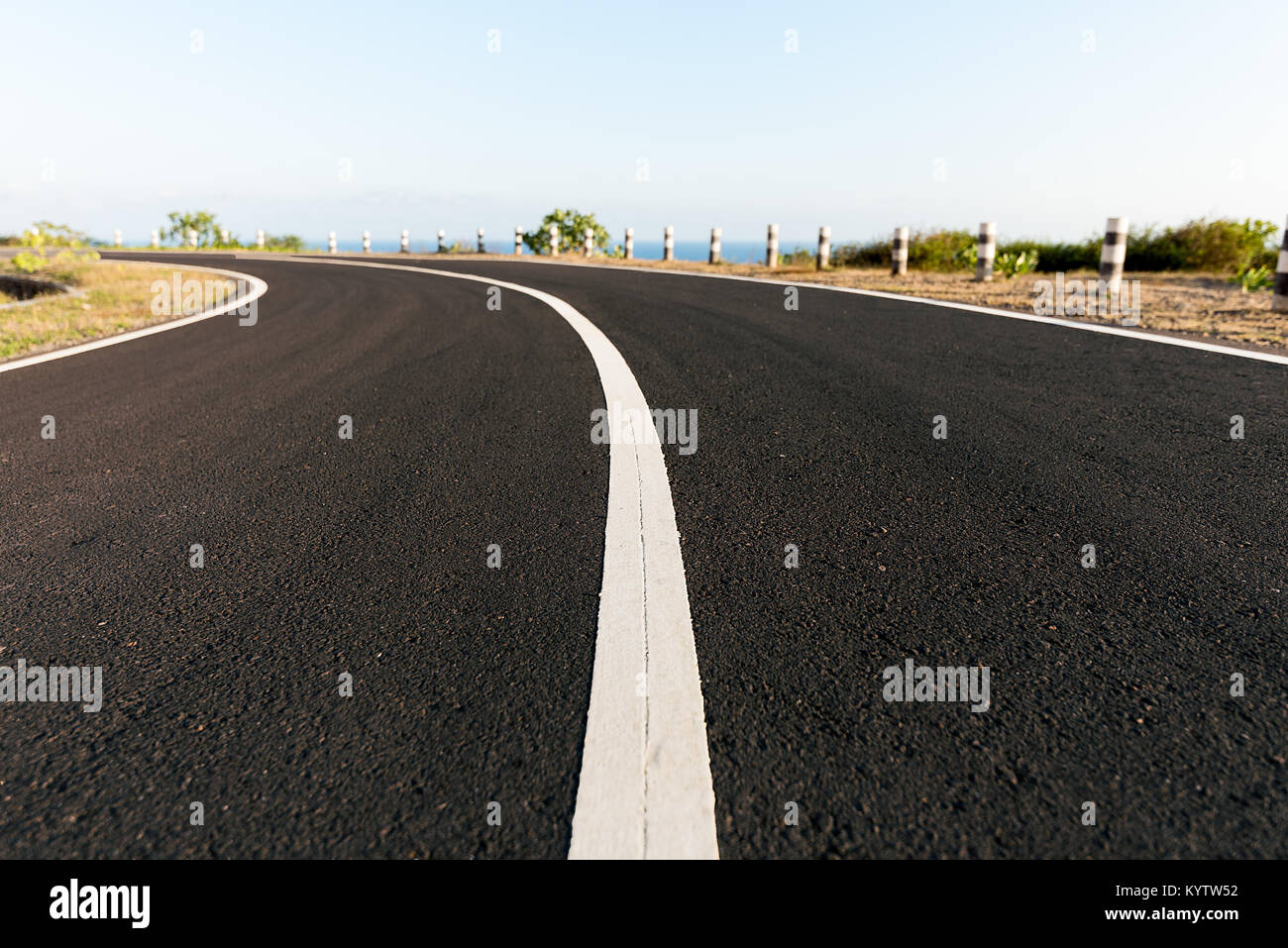 Tarmac coastal road going round cliff edge bend, with blue sea back drop. Stock Photo