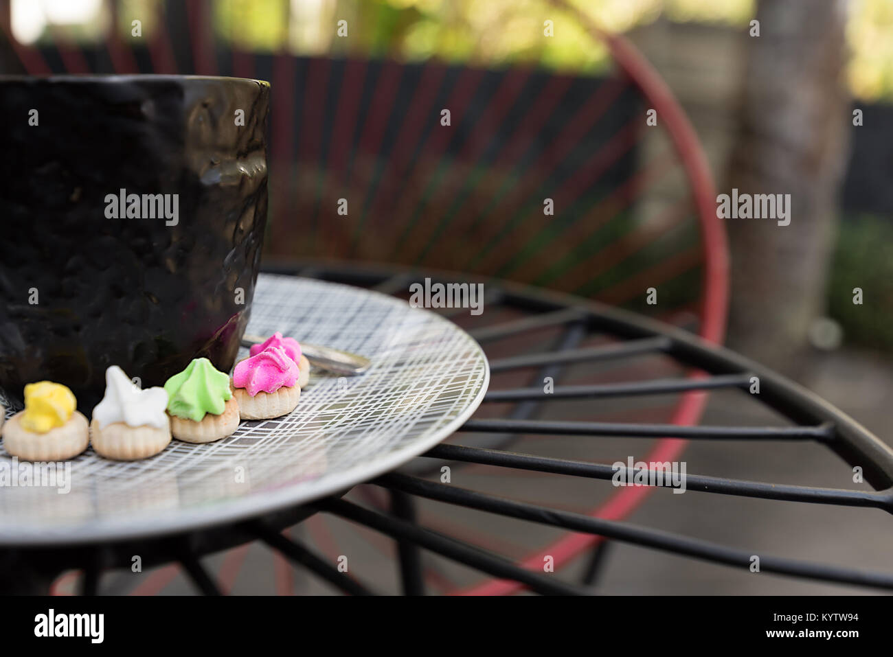 Hot Americano coffee with crema top in a classy black glass surrounded buy colourful classic Ice Gem sweets biscuits on a patterned plate. Stock Photo