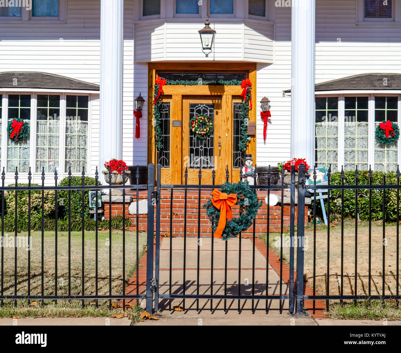 Entrance gate and porch of upscale house with tall pillars bay windows and leaded glass doors all decorated for Christmas with wreaths and bows and po Stock Photo
