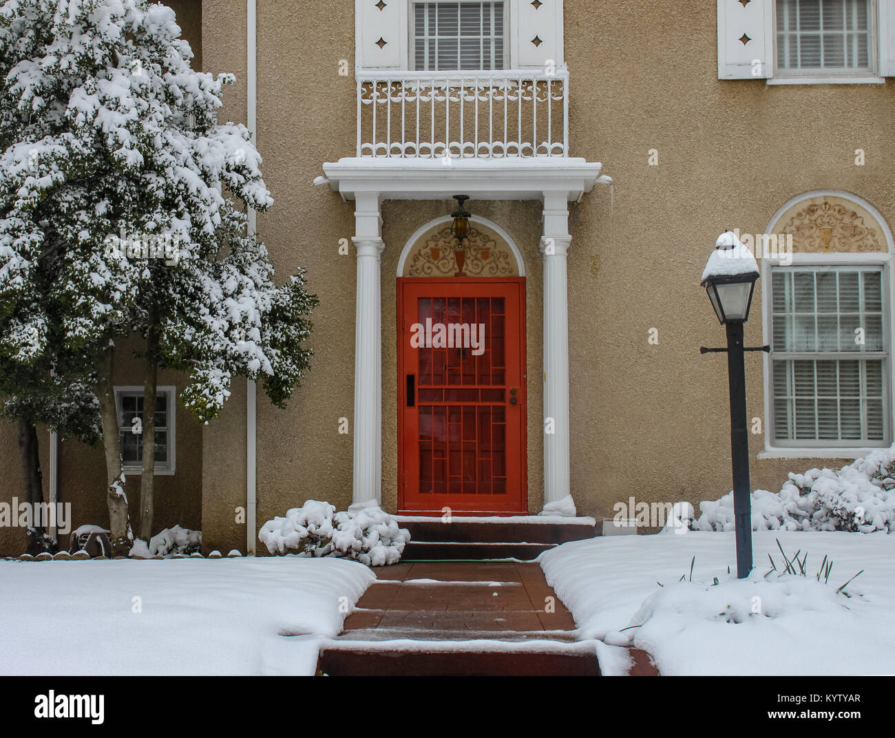 Entrance of elegant upscale stucco house with pillars and tiles in snow with bright red door and shoveled sidewalk Stock Photo