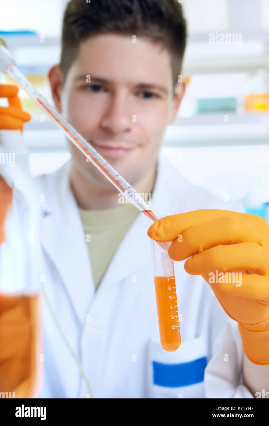 Young energetic scientist loads orange liquid sample in a tube. Scientific background, blurred face, focus on the tube. This image is toned. Stock Photo