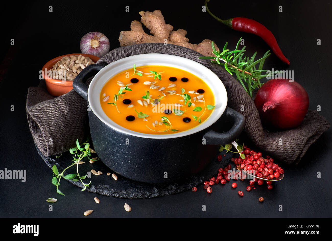 Spicy pumpkin creme soup served in ceramic pan with pumpkin oil, thyme leaves and sunflower