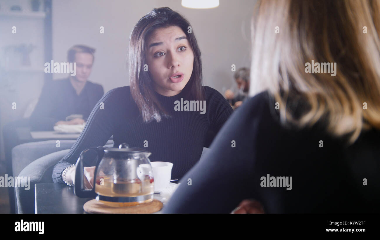 Black haired young woman with black hair drinking coffee and talking with  girlfriend in the cafe Stock Photo - Alamy