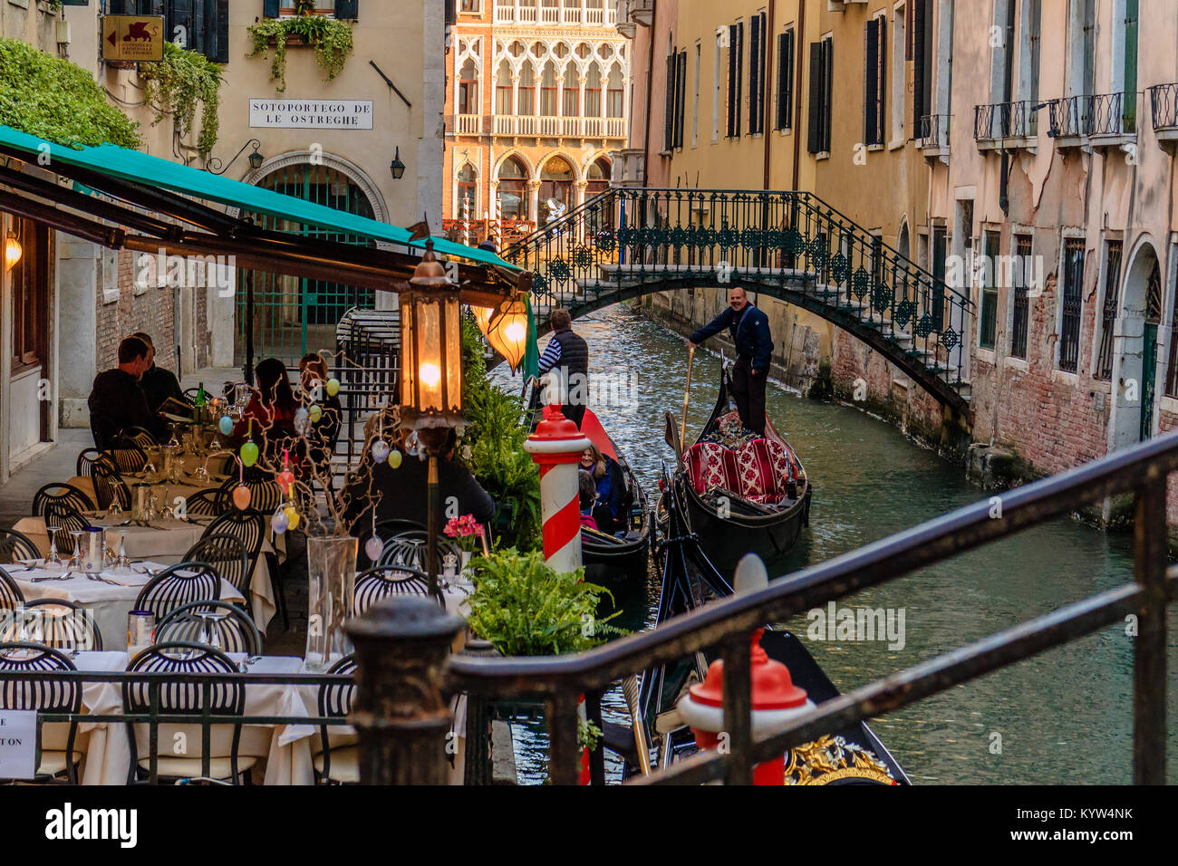 Man with a gondola passes an outdoor restaurant terrace by a canal in Venice, Italy. Stock Photo