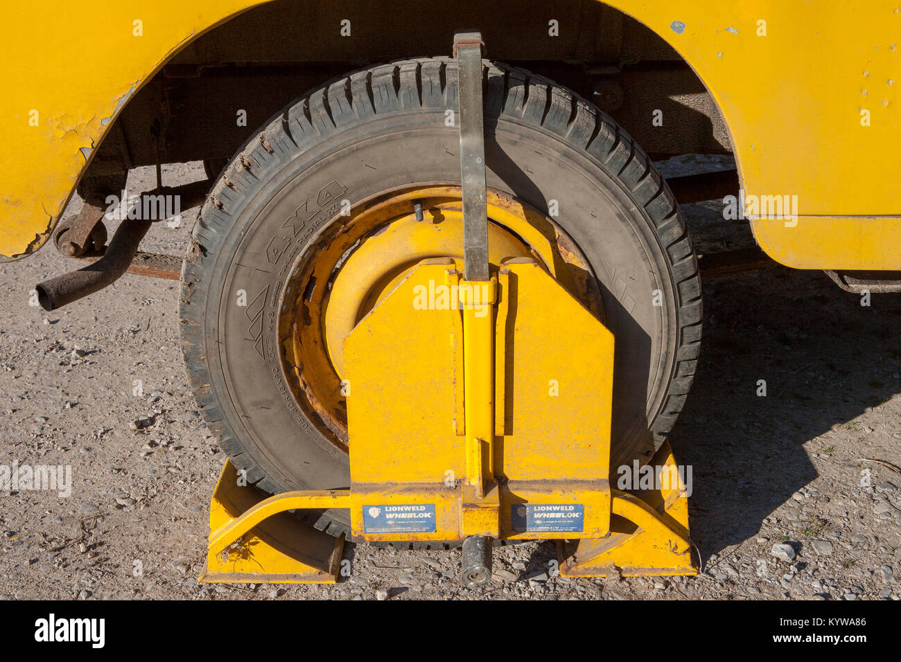A yellow wheel clamp on a yellow Land Rover Series 3. Parked on private