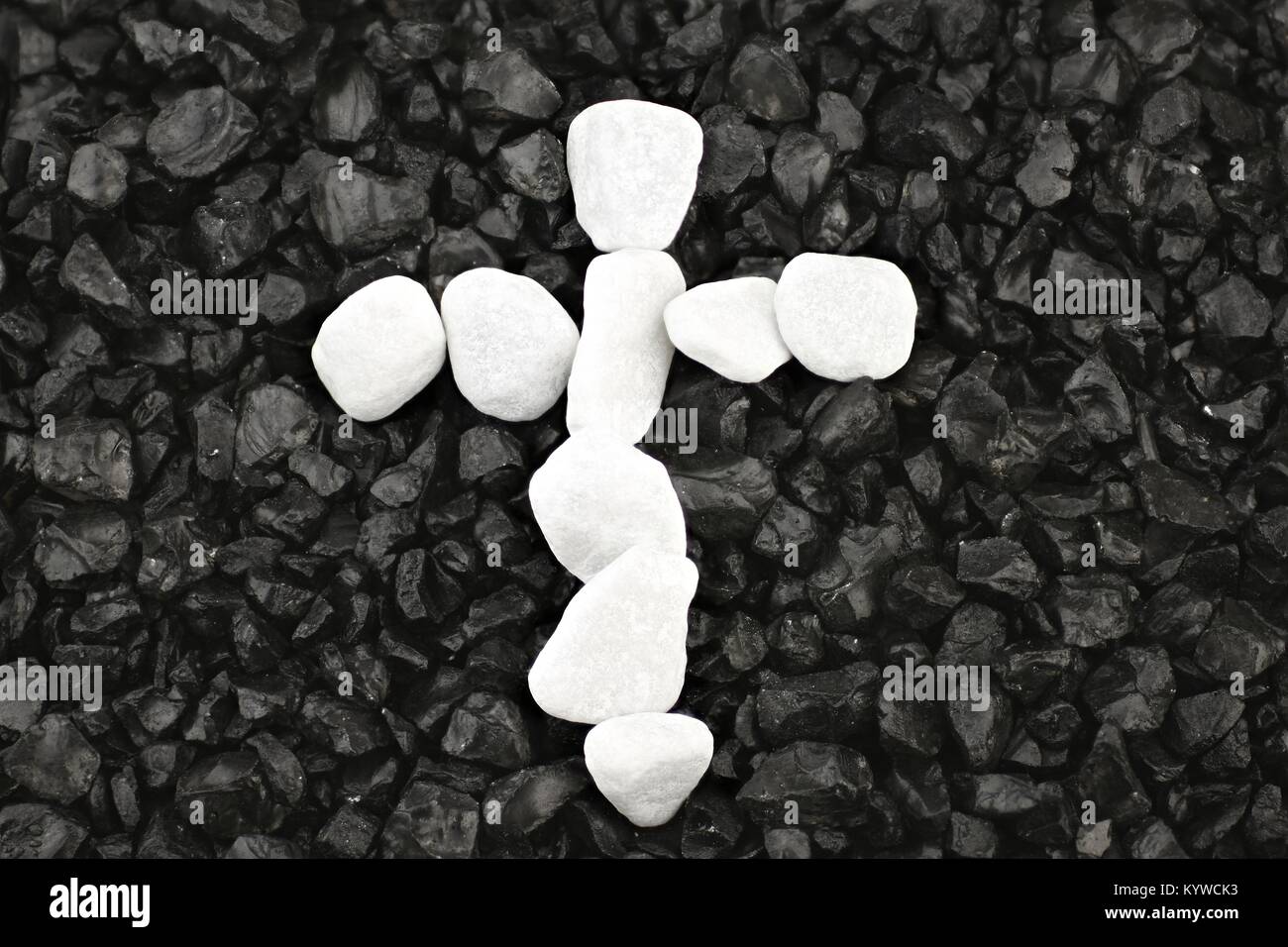 Cross of white pebbles against background of black grit Stock Photo