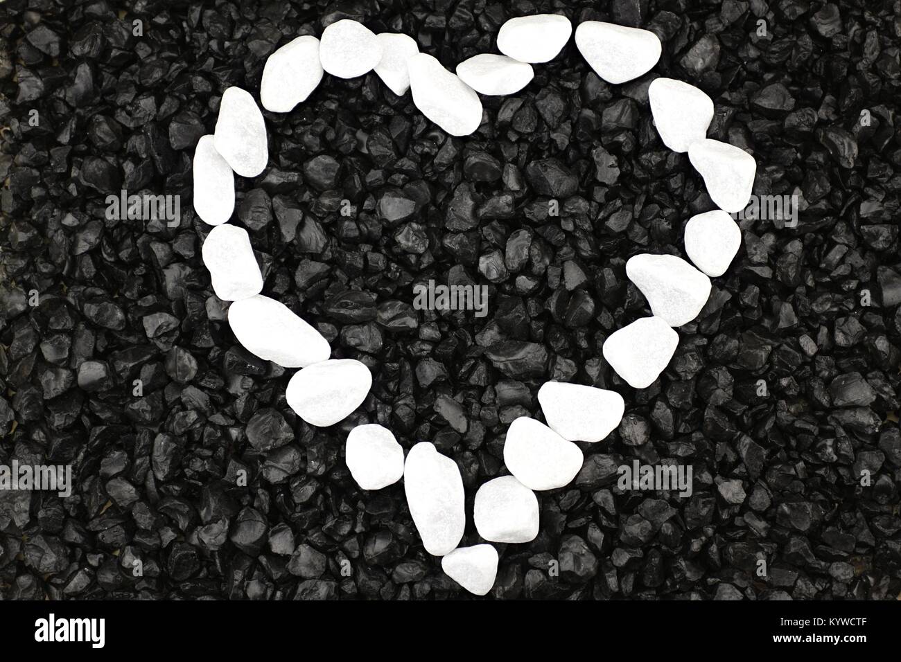 Heart of white pebbles against background of black grit Stock Photo