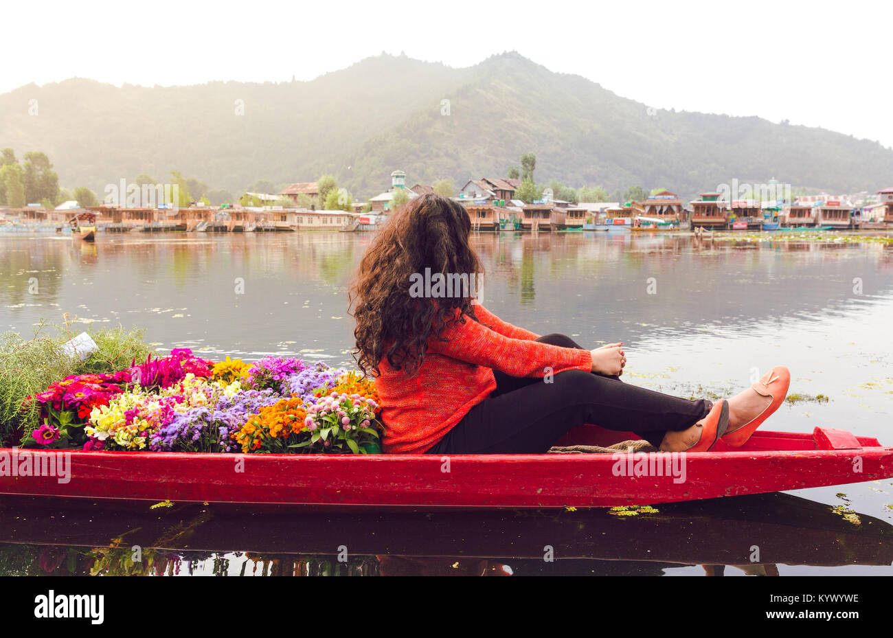 A Shikhara full of colorful flowers with a single travelling girl/woman. Backpacking girl on Dal lake, Srinagar, Kasmir, India. vibrant sunrise scene, Stock Photo