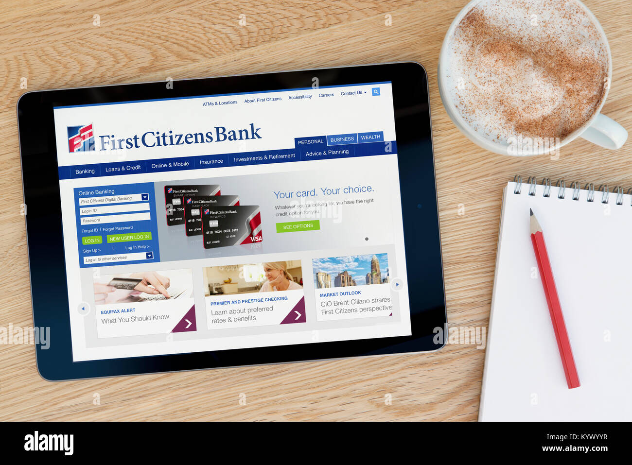 The First Citizens Bank website on an iPad tablet, on a wooden table beside a notepad, pencil and cup of coffee (Editorial only) Stock Photo