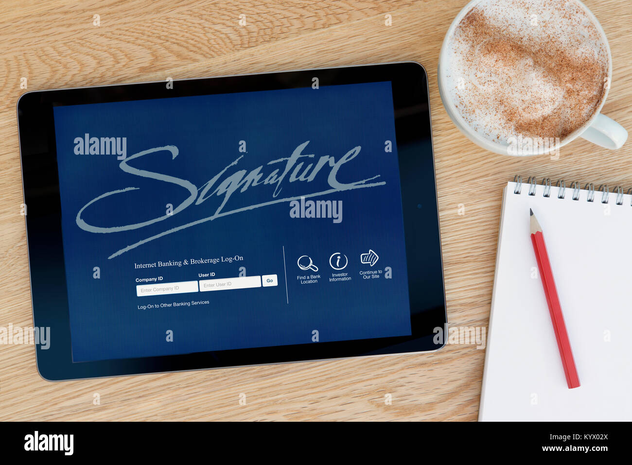The Signature Bank website on an iPad tablet, on a wooden table beside a notepad, pencil and cup of coffee (Editorial only) Stock Photo