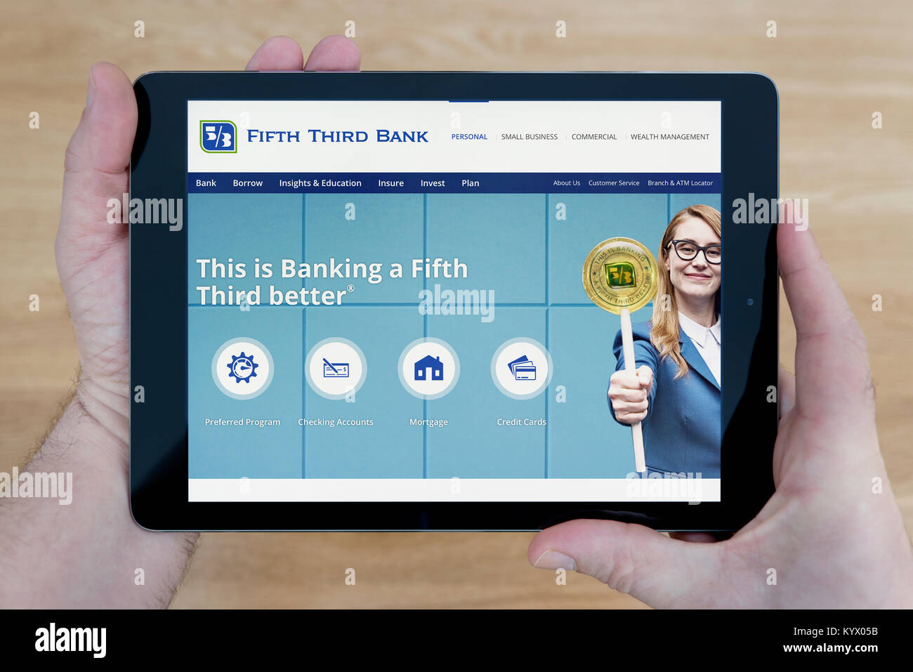 A man looks at the Fifth Third Bank website on his iPad tablet device, with a wooden table top background (Editorial use only) Stock Photo